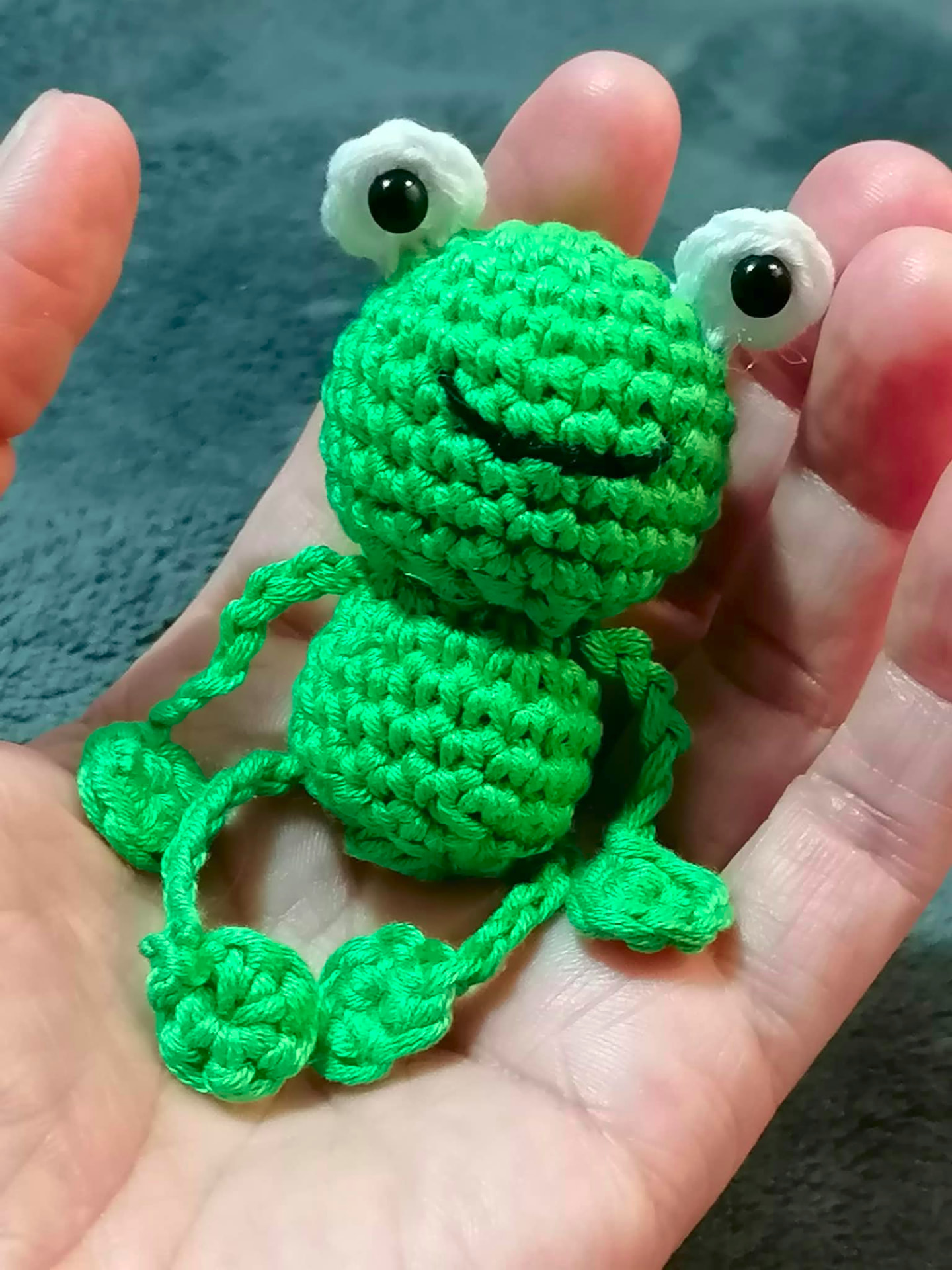 A miniature green crocheted frog held in the palm of a hand