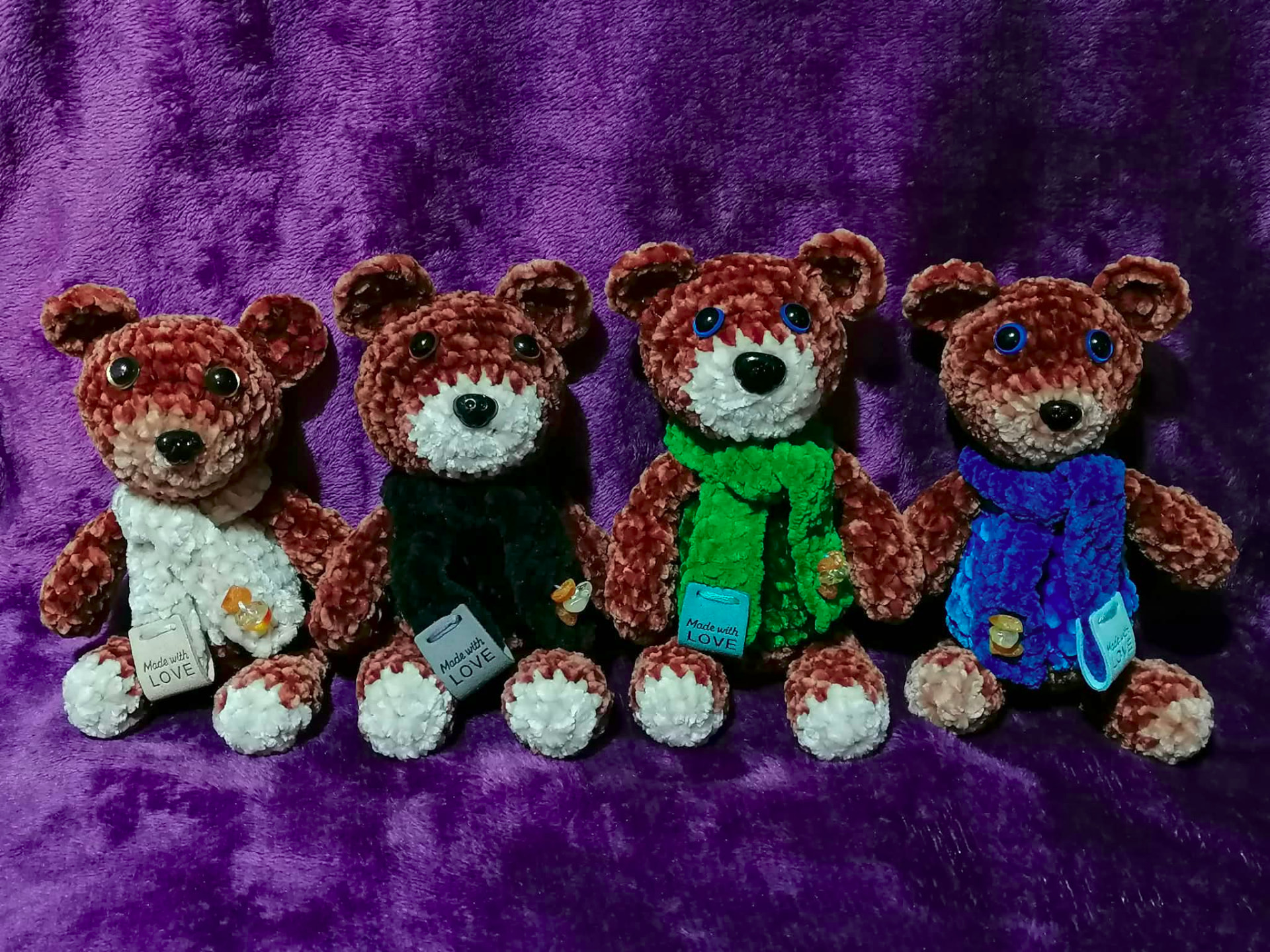 Four handmade crocheted teddy bears in matching brown tones wearing white, black, green and blue scarves