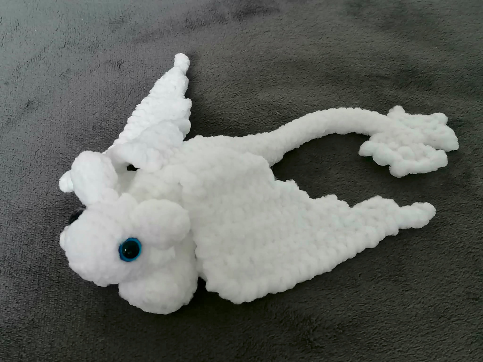 A handmade crocheted dragon in light colours