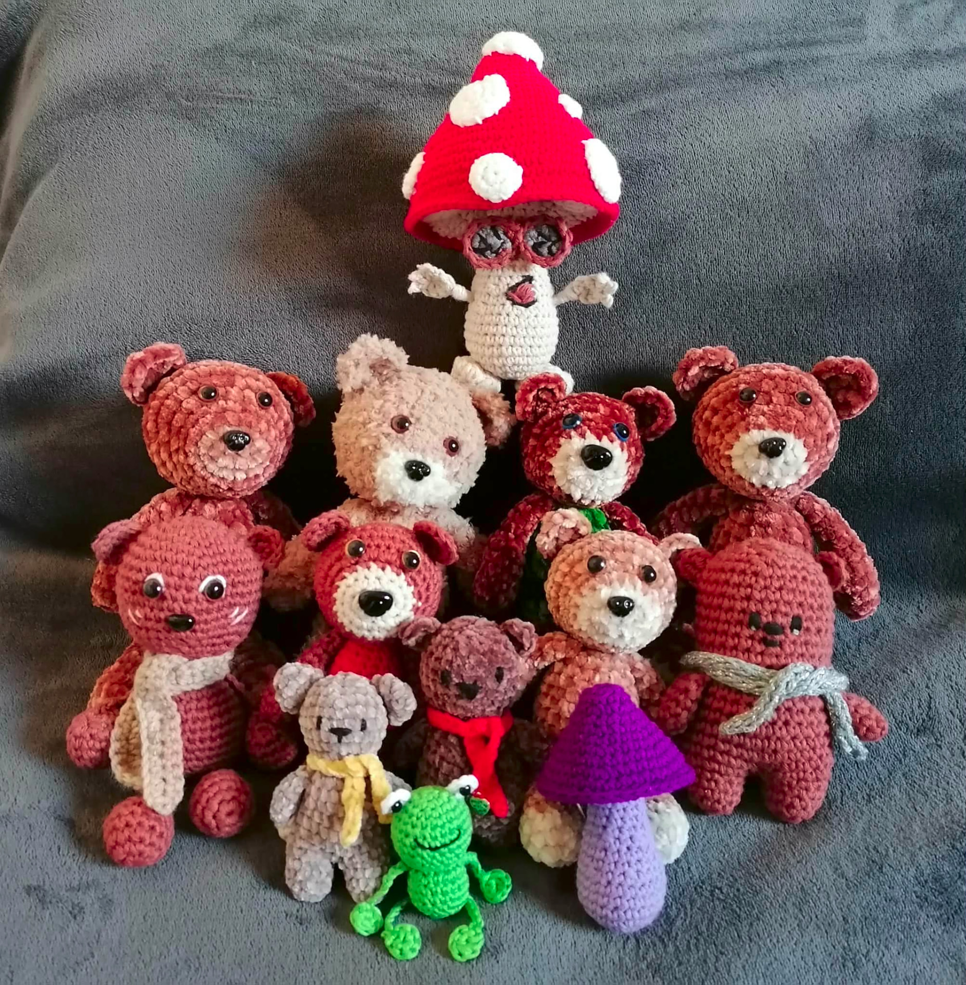 A group of handmade crocheted teddy bears, a small frog and mushroom characters gathered together