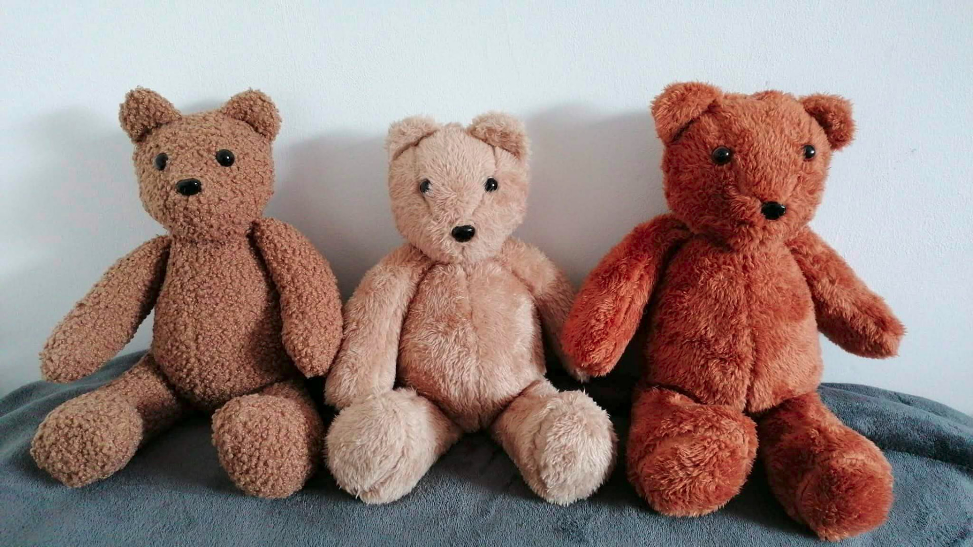 Three machine-sewn plush teddy bears in brown, cream and red fabrics sitting side by side
